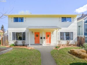 N Albina Duplex Cream, with coral pink doors and green lawn. 4 windows on front and cute wreaths on doors