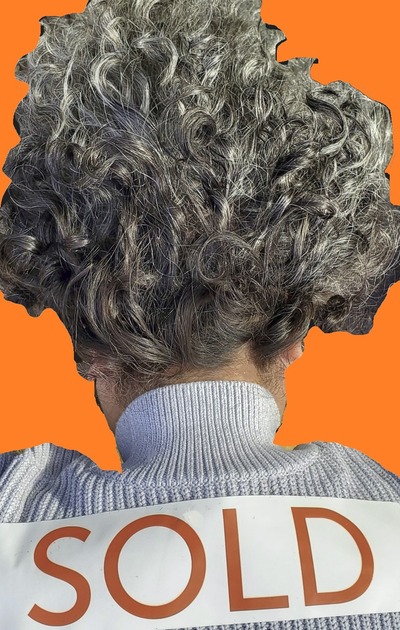 A Realtor from behind with grey curly hair which is standing on end in front of an orange background. Sweater has a "SOLD" sticker on it - implying how hair-raising the Portland market is.