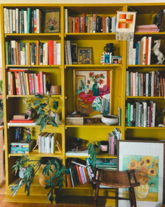 wood bookshelf filled with plants, books, and art